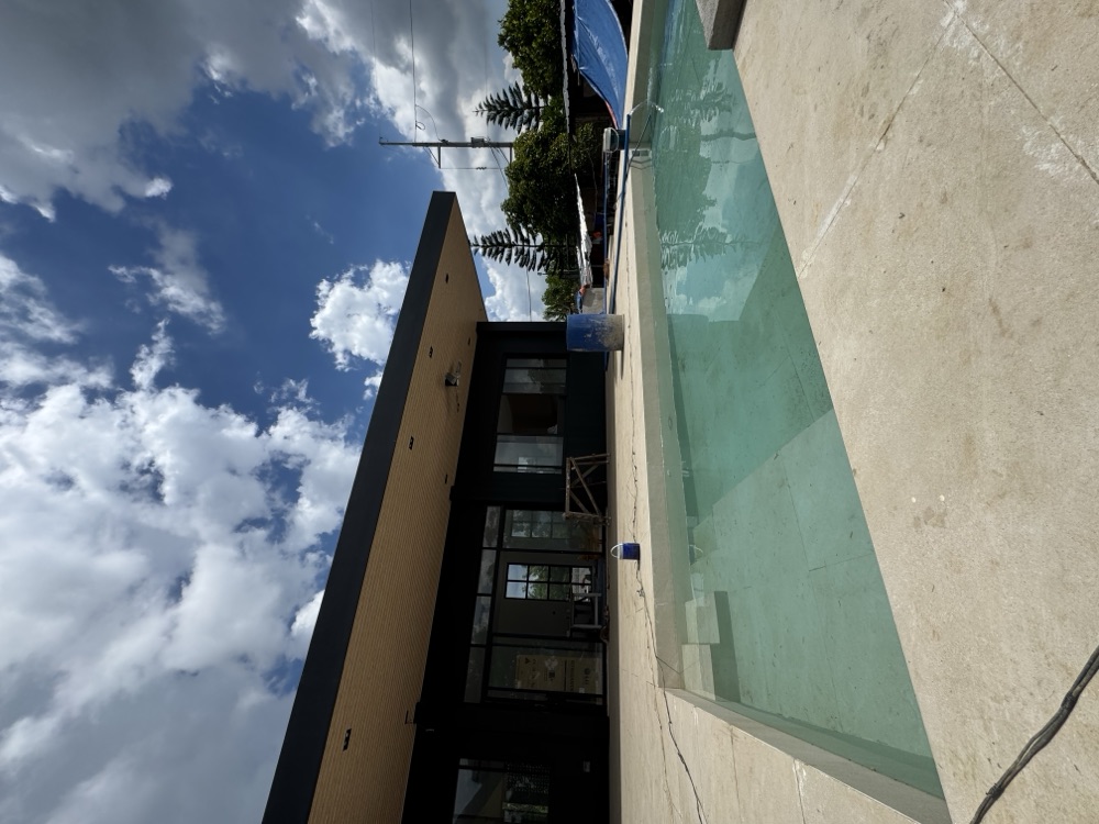 Maison Adriana mid-construction — dark single-storey facade under a deep timber soffit, with the pool filled.