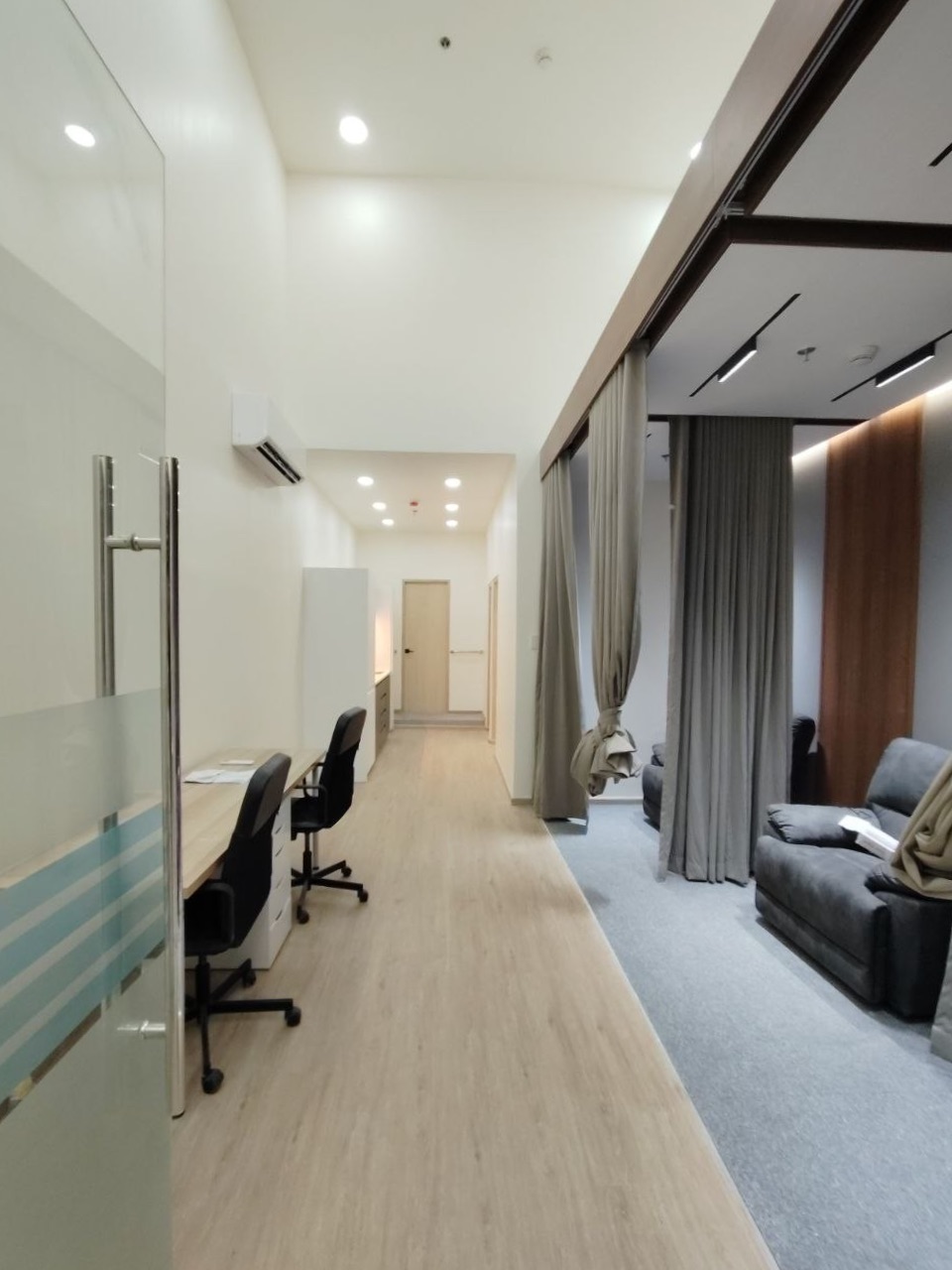 OPAT Health — the infusion bay behind curtain tracks, seen from the glazed circulation spine.
